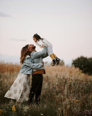 Parents lifting their child into the air in a sunlit meadow