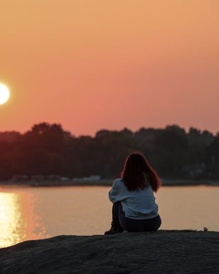 Someone sitting quietly by a lake at sunrise
