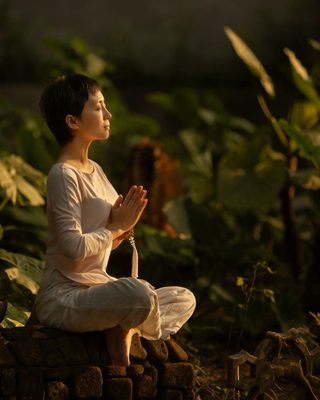 A woman meditating among green plants