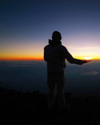 A person on a mountain at sunrise, arm outstretched